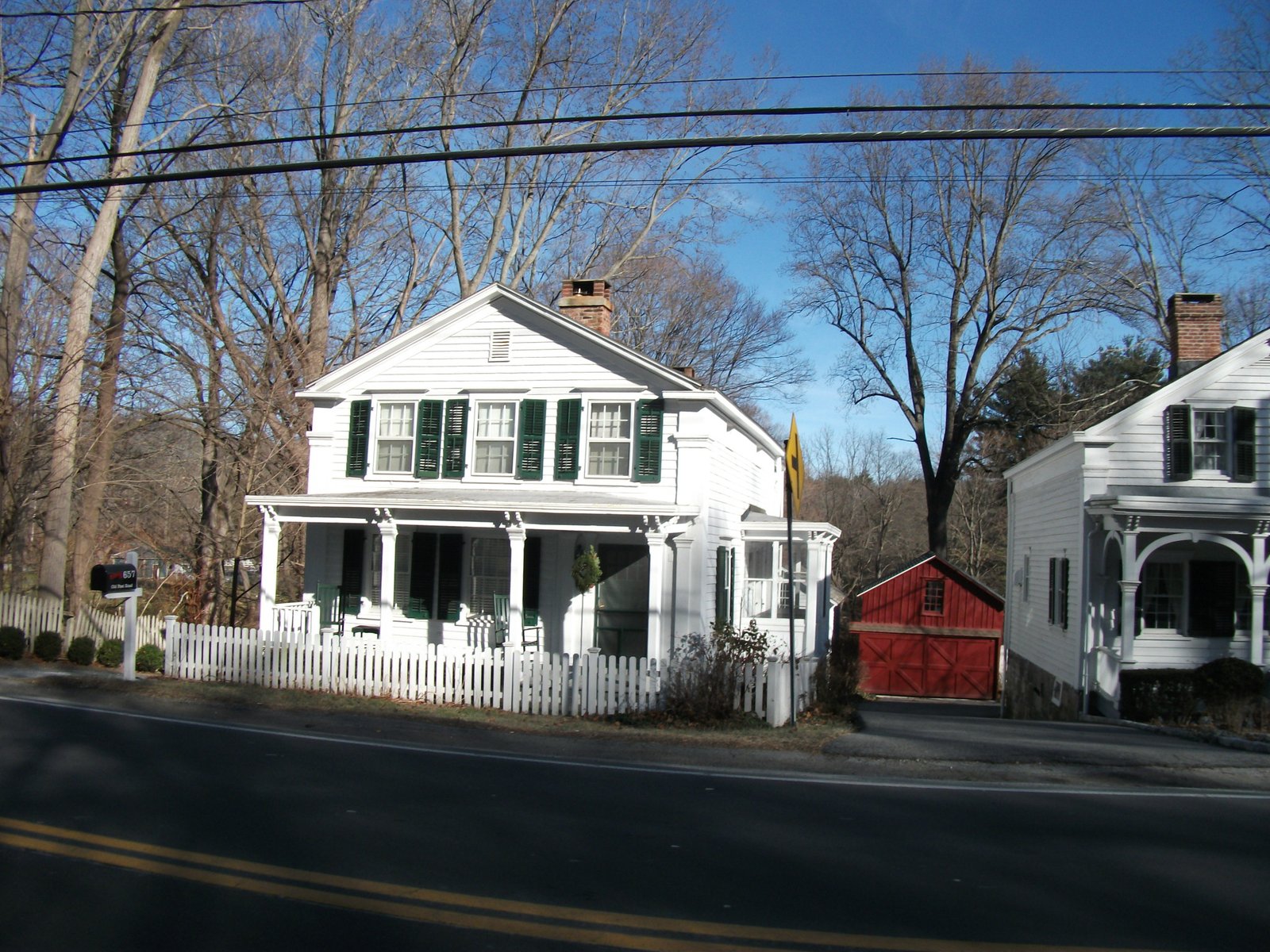 Empty roadside view of white clapboard houses, a picket fence and a red barn-style garage in the Bedford Village Historic District, Bedford, NY, with no people, Westchester County