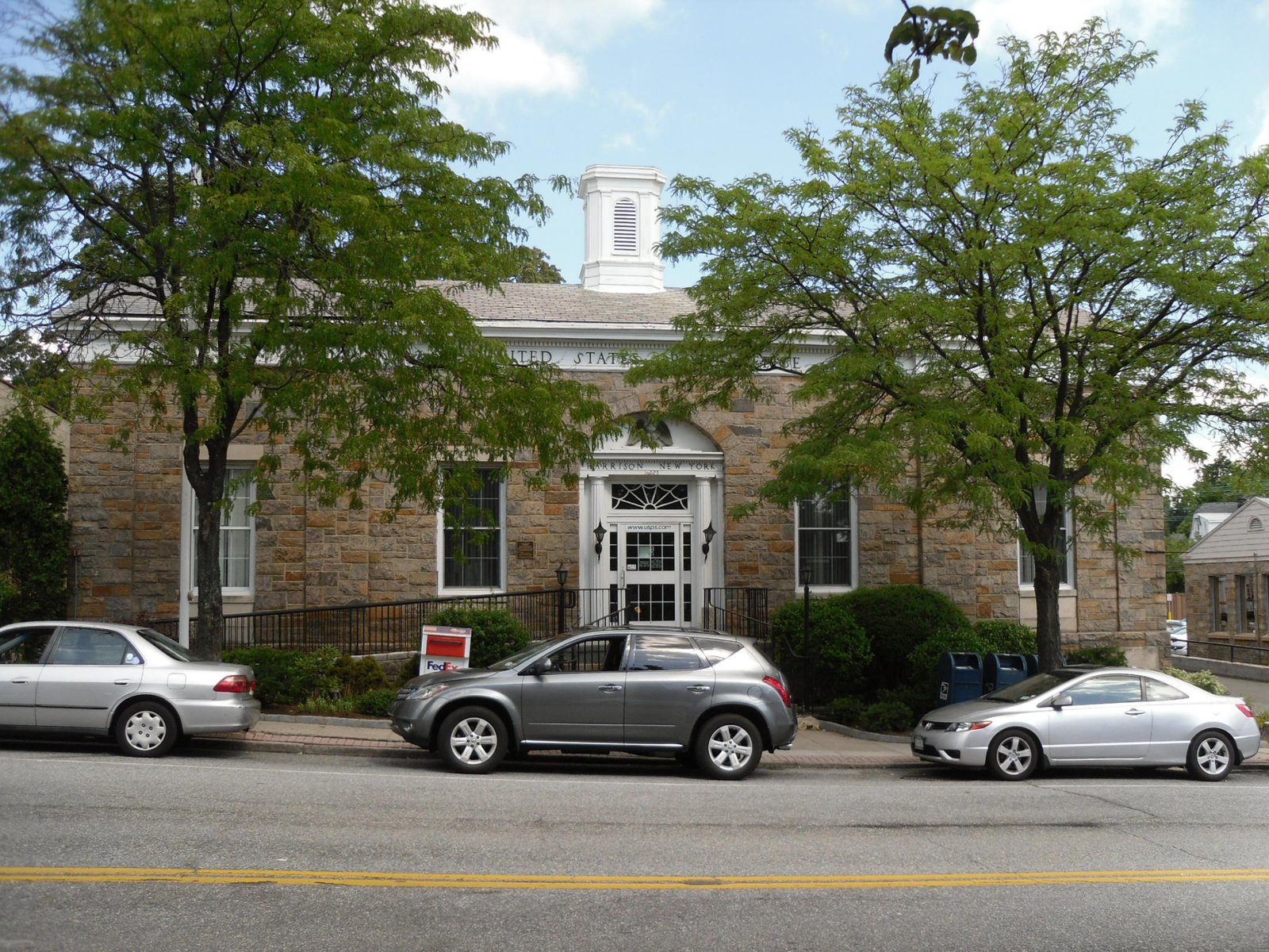 Empty front of the stone U.S. Post Office building on a Harrison, NY street with parked cars and no people, Westchester County